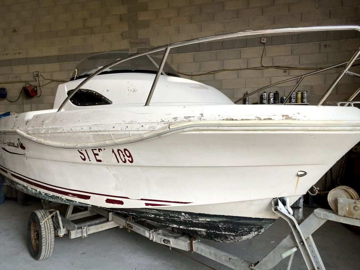 Coque de bateau blanche arrivée à l’atelier SAM BOAT, gelcoat écaillé sur le bord et carène usée